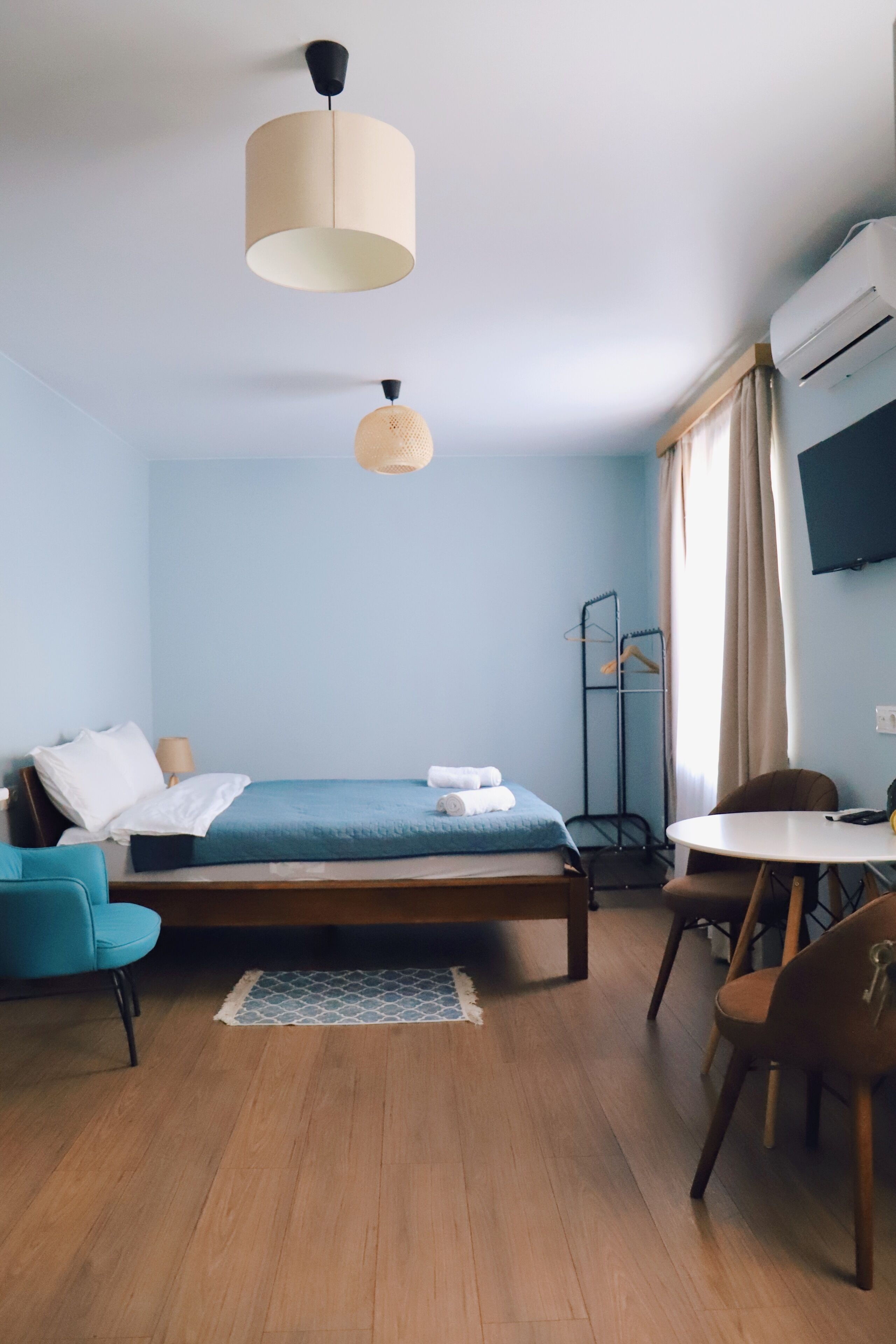 A room with a bed, a desk, and a chair. There is a hanging light fixture above the bed.
