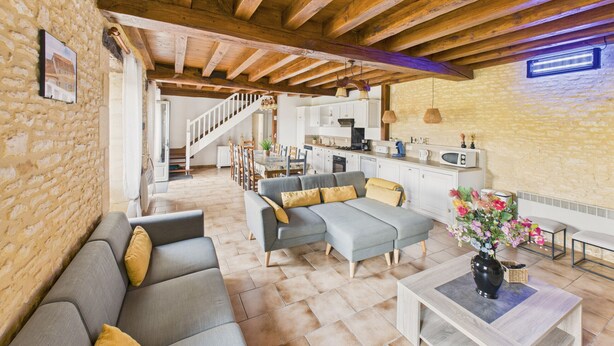 A spacious living area with a grey sectional sofa, a wooden coffee table, and a kitchen in the background. - Beautiful gîte for 12 with garden and terrace (Saint-Crépin-et-Carlucet)