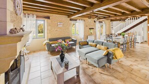 A spacious living room with a fireplace, two sofas, a coffee table, and a dining area with a staircase. - Beautiful gîte for 12 with garden and terrace (Saint-Crépin-et-Carlucet)