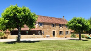 A stone house with a tiled roof, a covered porch, and a well-maintained lawn. - Beautiful gîte for 12 with garden and terrace (Saint-Crépin-et-Carlucet)