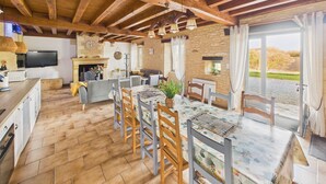 A spacious kitchen with wooden beams, a dining area with a table and chairs, a television, and a stone wall. - Beautiful gîte for 12 with garden and terrace (Saint-Crépin-et-Carlucet)