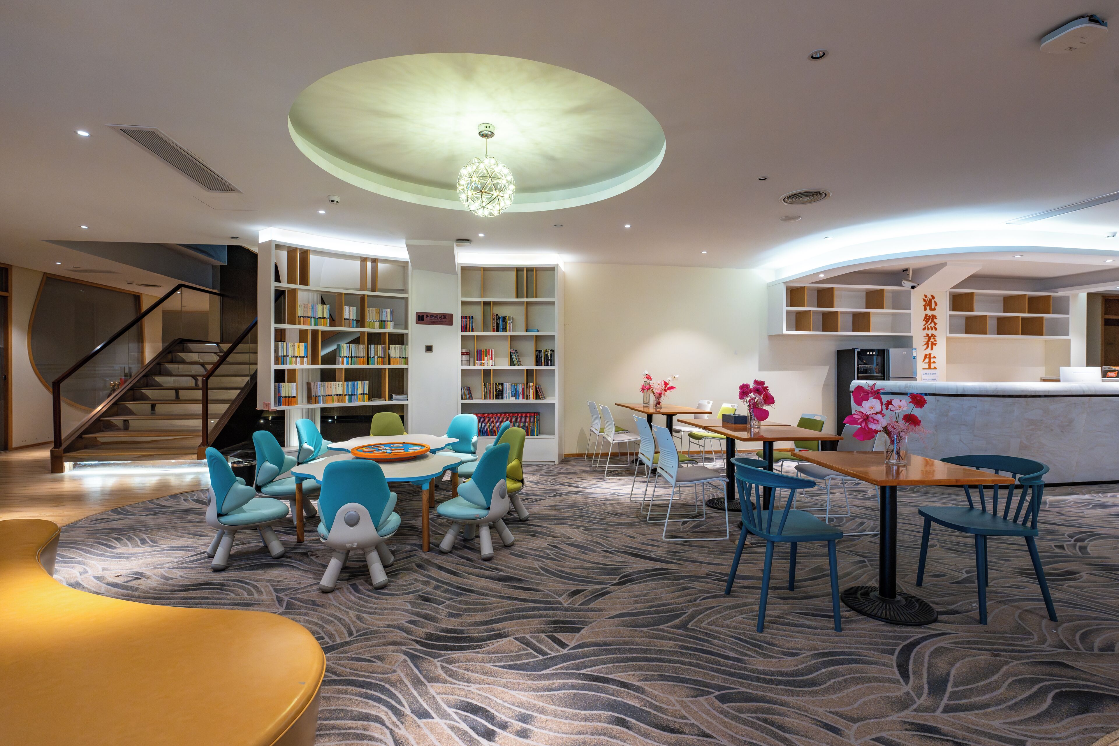 Un moderno vestíbulo de hotel con una escalera curva, una zona de juegos para niños, una recepción y una biblioteca.
