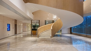 A modern interior with a curved wooden staircase, a large potted plant, and a reflective floor. - Castfast Hotel (Dongguan)