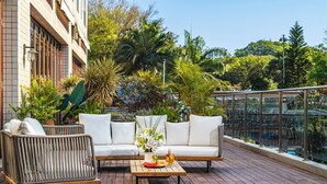 A rooftop terrace with a white sofa, wicker chair, and a table with a drink and fruit. - Castfast Hotel (Dongguan)