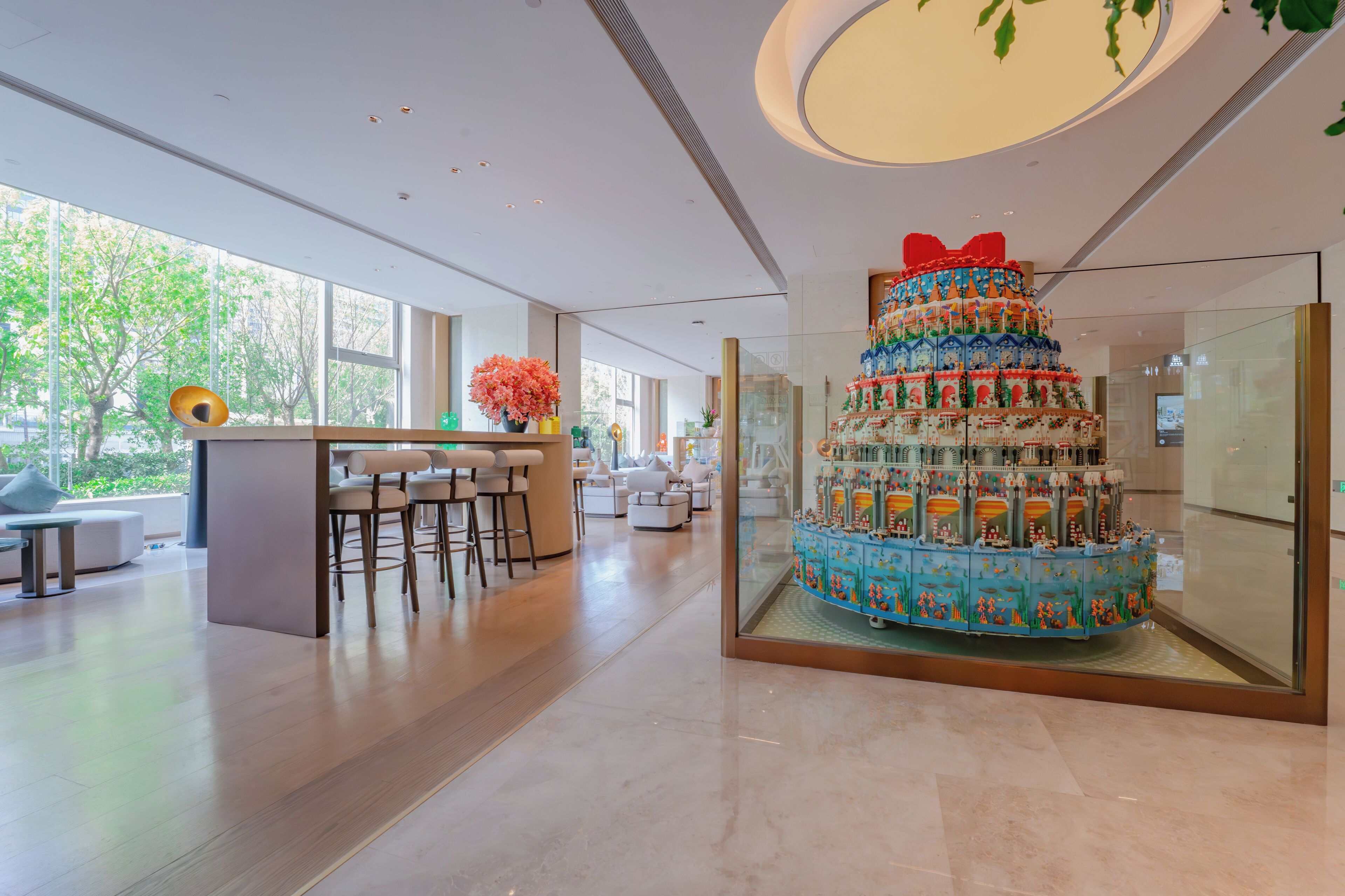 A modern hotel lobby with a central bar area, seating, and a large decorative cake centerpiece.
