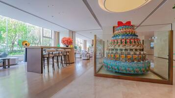A modern hotel lobby with a central bar area, seating, and a large decorative cake centerpiece.