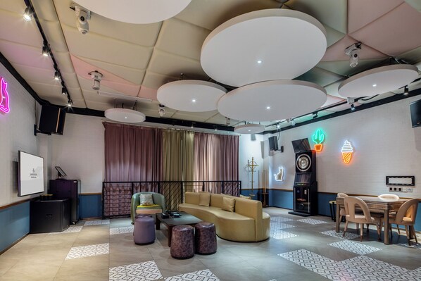 A modern lounge area with a sofa, coffee table, and stools, a clock, and a neon ice cream sign. - Castfast Hotel (Dongguan)