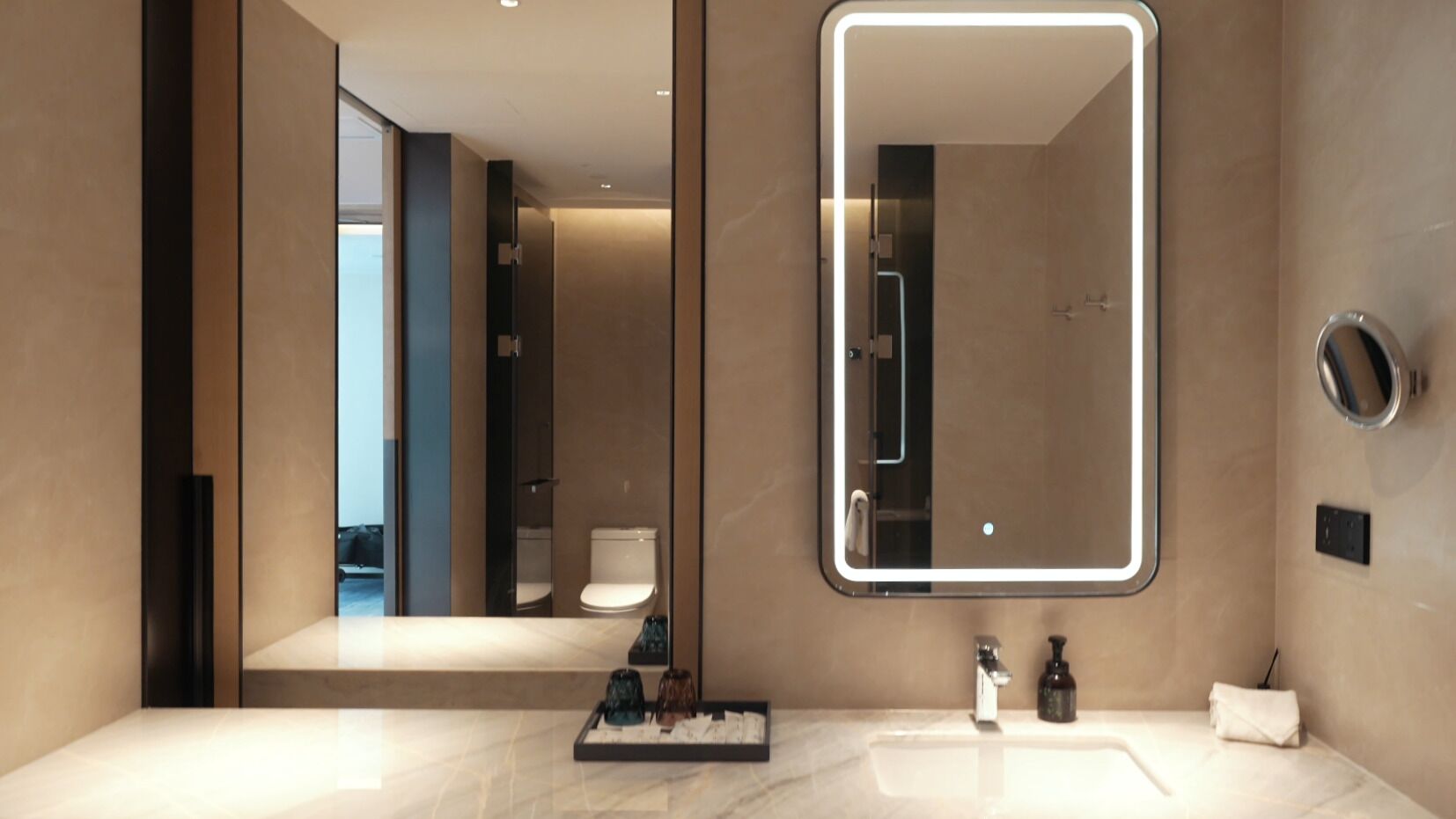 A modern bathroom with a large mirror, a marble countertop, and a visible shower area.