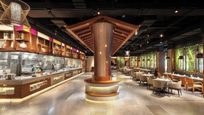 A modern restaurant with a central wooden column, a counter with a display case, and multiple dining tables. - Castfast Hotel (Dongguan)
