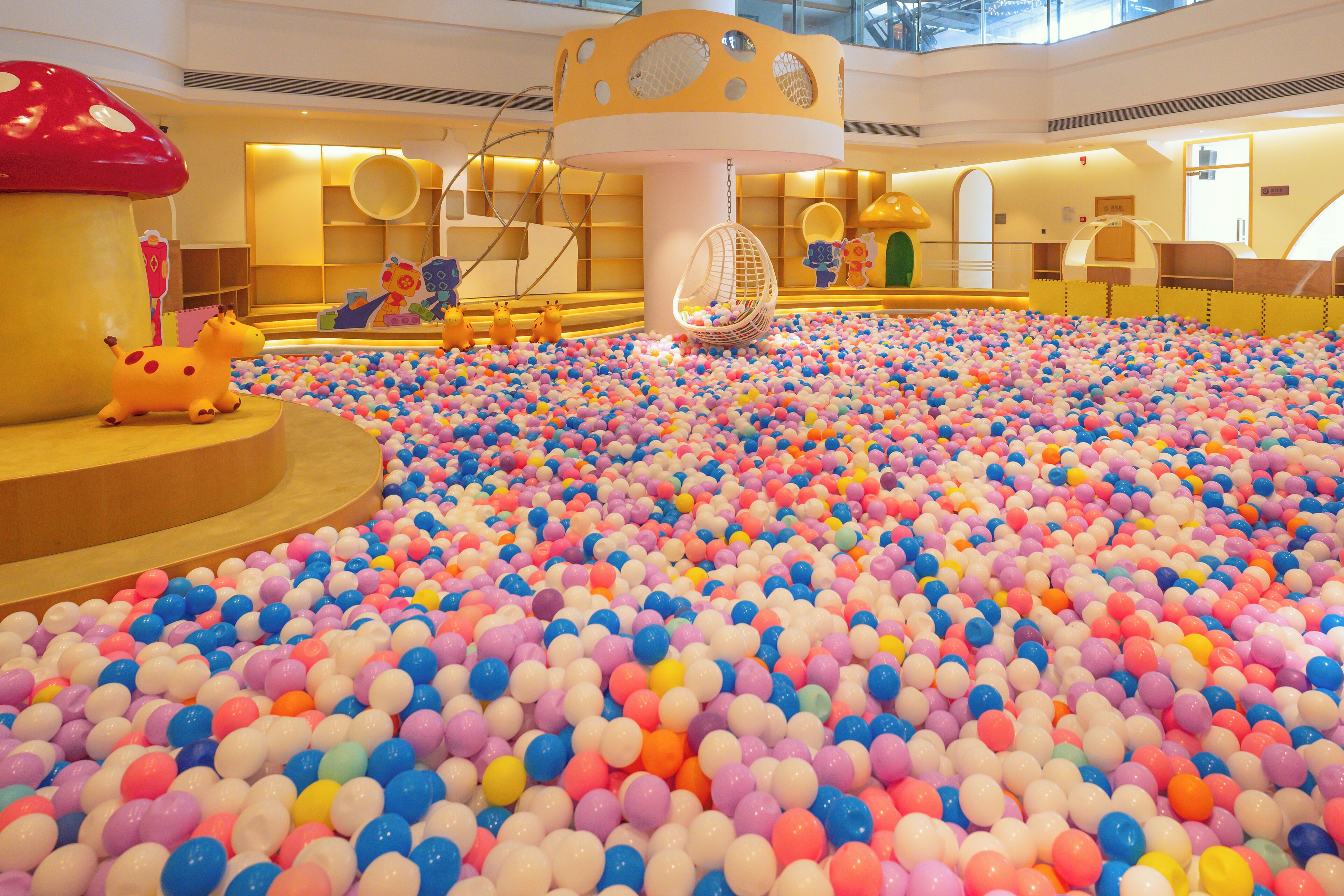 A large indoor play area with a ball pit filled with multicolored balls, a hanging swing, and playful animal sculptures.