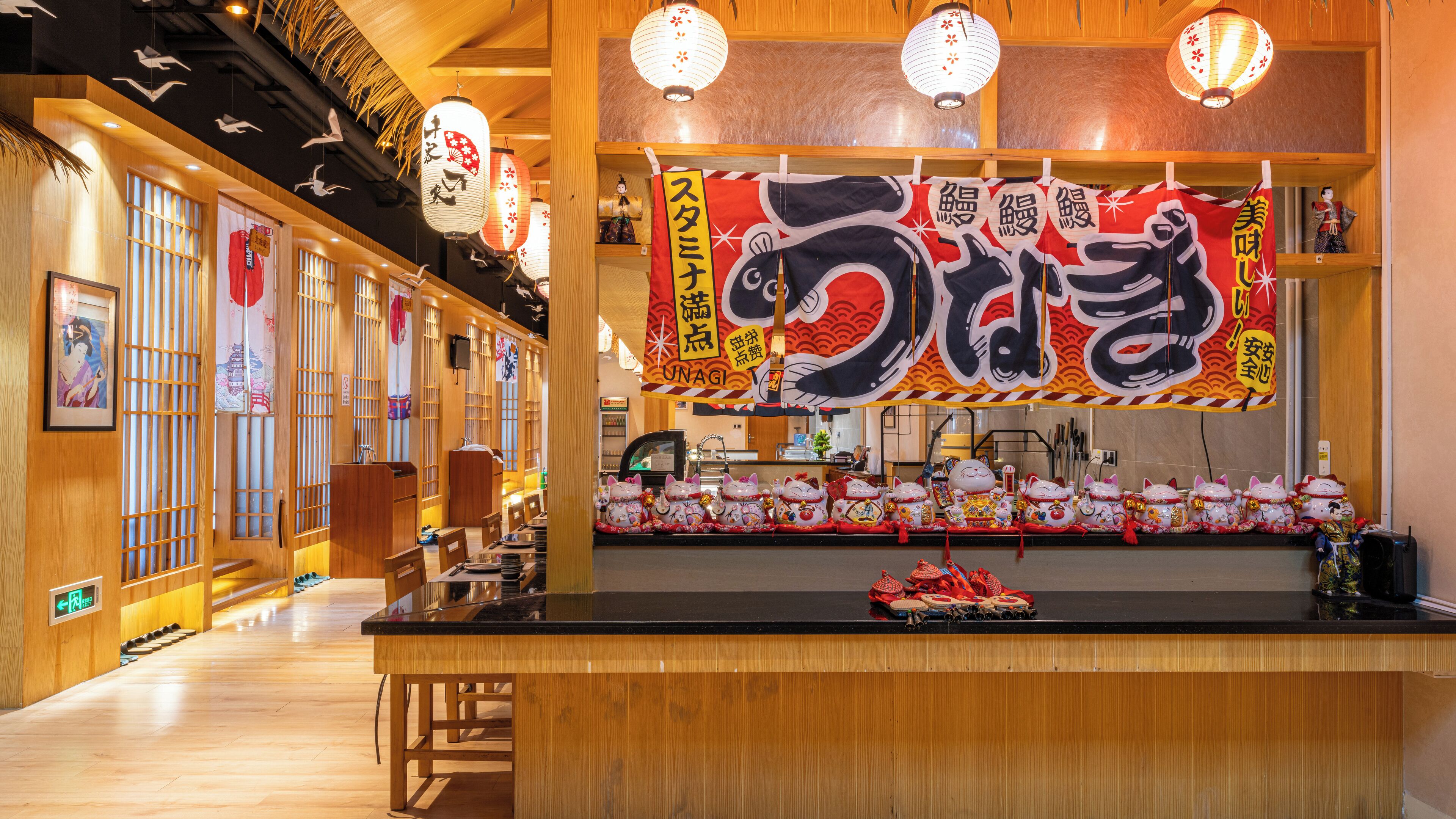 A traditional Japanese restaurant interior with wooden decor, a counter with cat-shaped decorations, and hanging lanterns.