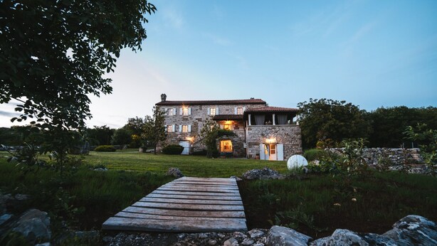 A stone house with a wooden deck leading to the entrance, surrounded by greenery and a stone wall. - Stancia Vigini by Villas Guide (Grožnjan)