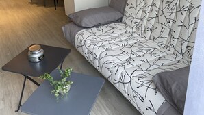 Een moderne woonkamer met een bank, een klein tafeltje met een plant en een eethoek met een gele tafelkleed.