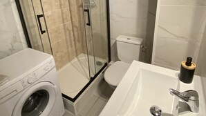 Een moderne badkamer met een douchecabine van glas, een witte wasmachine en een wastafel met een zwarte zeepdispenser.