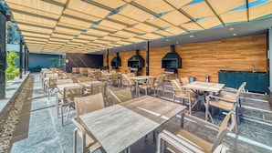 Un amplio espacio exterior con mesas y sillas, un muro de madera y un diseño moderno del techo.
