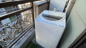 Eine Waschmaschine auf einem Balkon mit Metallgeländer.