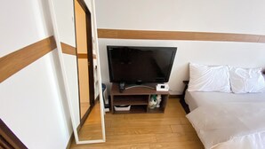 Ein Hotelzimmer mit einem Bett, einem Fernseher auf einem Holzständer, einer Fernbedienung und einem weißen Kissen.