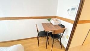 Ein kleiner Raum mit einem Holztisch, zwei Stühlen, einem weißen Korb und einem kleinen Blumentopf.