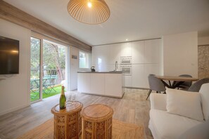 A modern kitchen with white cabinets, a dining area with a wooden table and chairs, and a large window overlooking a garden. - 2 Bedrooms Balcony garden view-Carnot A2B266 (Cannes)