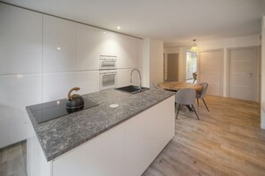 Cuina moderna amb armaris blancs, tauleig de granat i una papereta. Hi ha una zona de dinar amb taula i cadires de fusta.