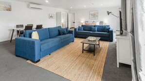 Ein modernes Wohnzimmer mit zwei blauen Sofas, einem Couchtisch und einem Essbereich mit Tisch und Stühlen.