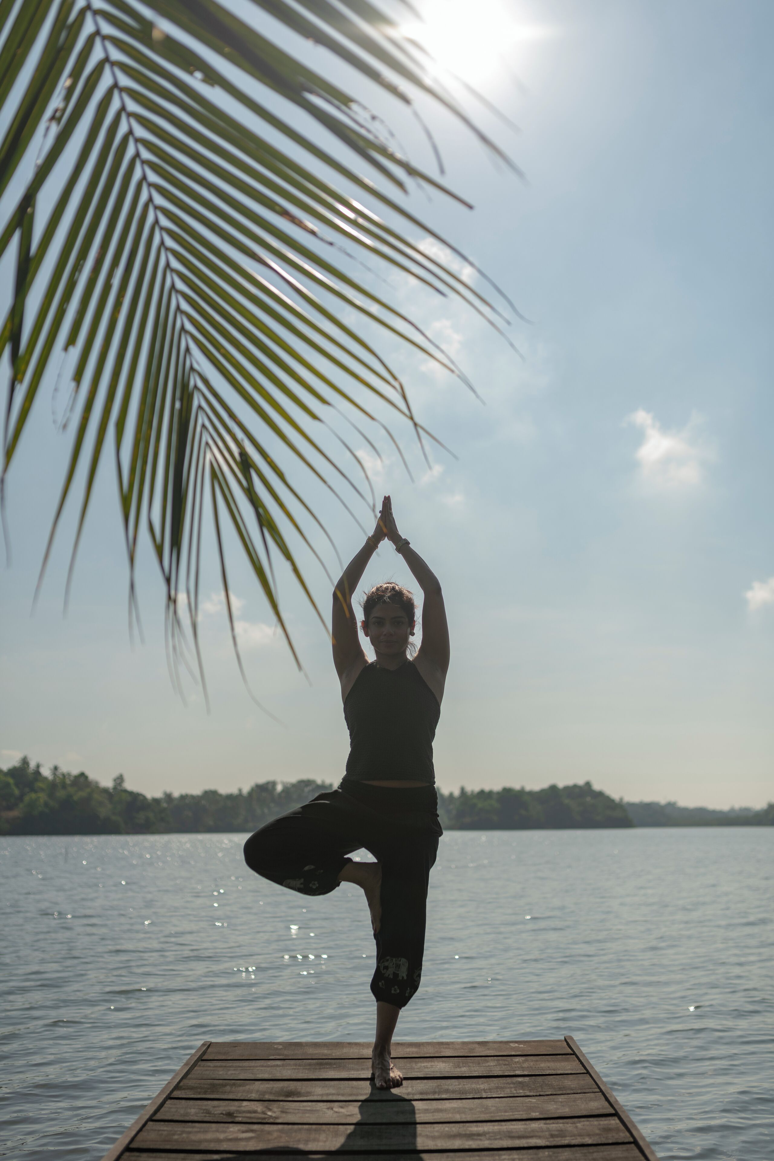 A person performing a yoga pose on a wooden dock by a calm lake with a clear sky.