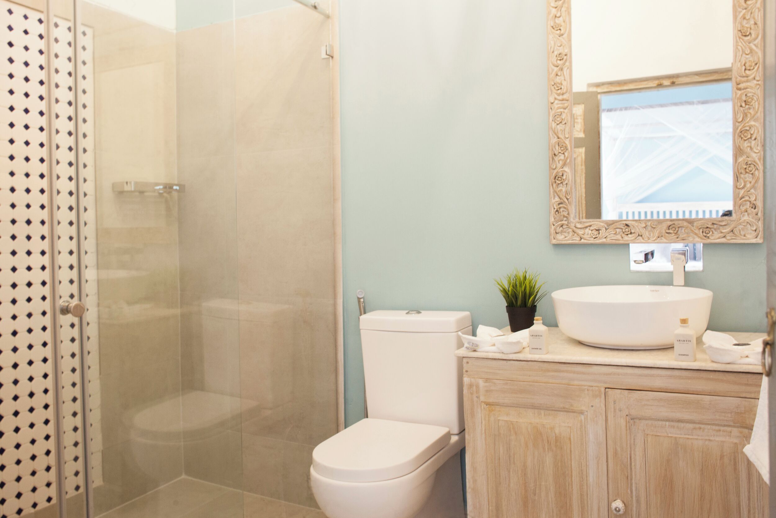 Une salle de bain avec une douche à parois de verre, des toilettes, un lavabo avec un grand miroir et un meuble contenant des articles de toilette.