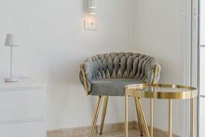 A modern room with a tufted grey chair, a small round table with gold legs, and a white lamp on a white console. - Apartment with an Ocean View and a Summery Atmosphere (Playa de las Américas)
