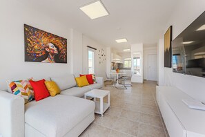 A modern living room with a white sofa, colorful pillows, a painting, and a dining area in the background. - Apartment with an Ocean View and a Summery Atmosphere (Playa de las Américas)