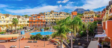A resort with a swimming pool, outdoor seating, and a mountainous backdrop.
