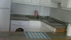 Cocina compacta con lavadora, lavaplatos y estufa. Hay dos taburetes y una mesa pequeña con un mantel de estampado de cuadrícula.