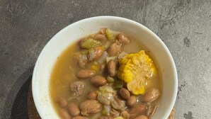 Un tazón de sopa con frijoles, maíz y verduras sobre un posavasos.