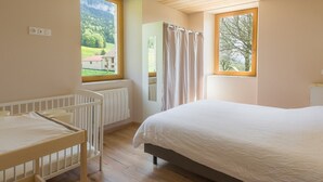 Een slaapkamer met een ledikant, een bed, een raam met uitzicht op groen, en een radiator.
