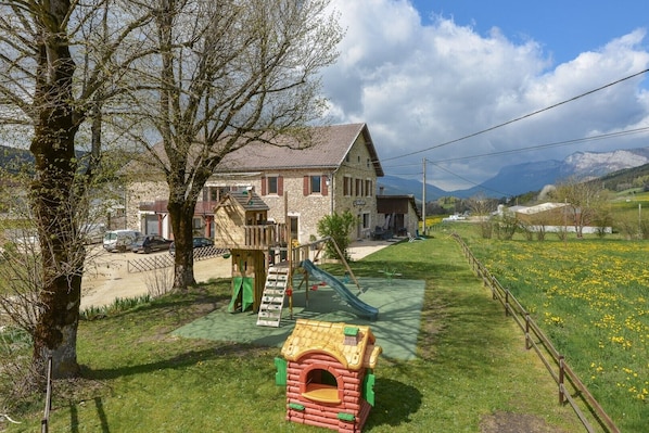 A stone house with a playground, a fenced yard, and a view of mountains.