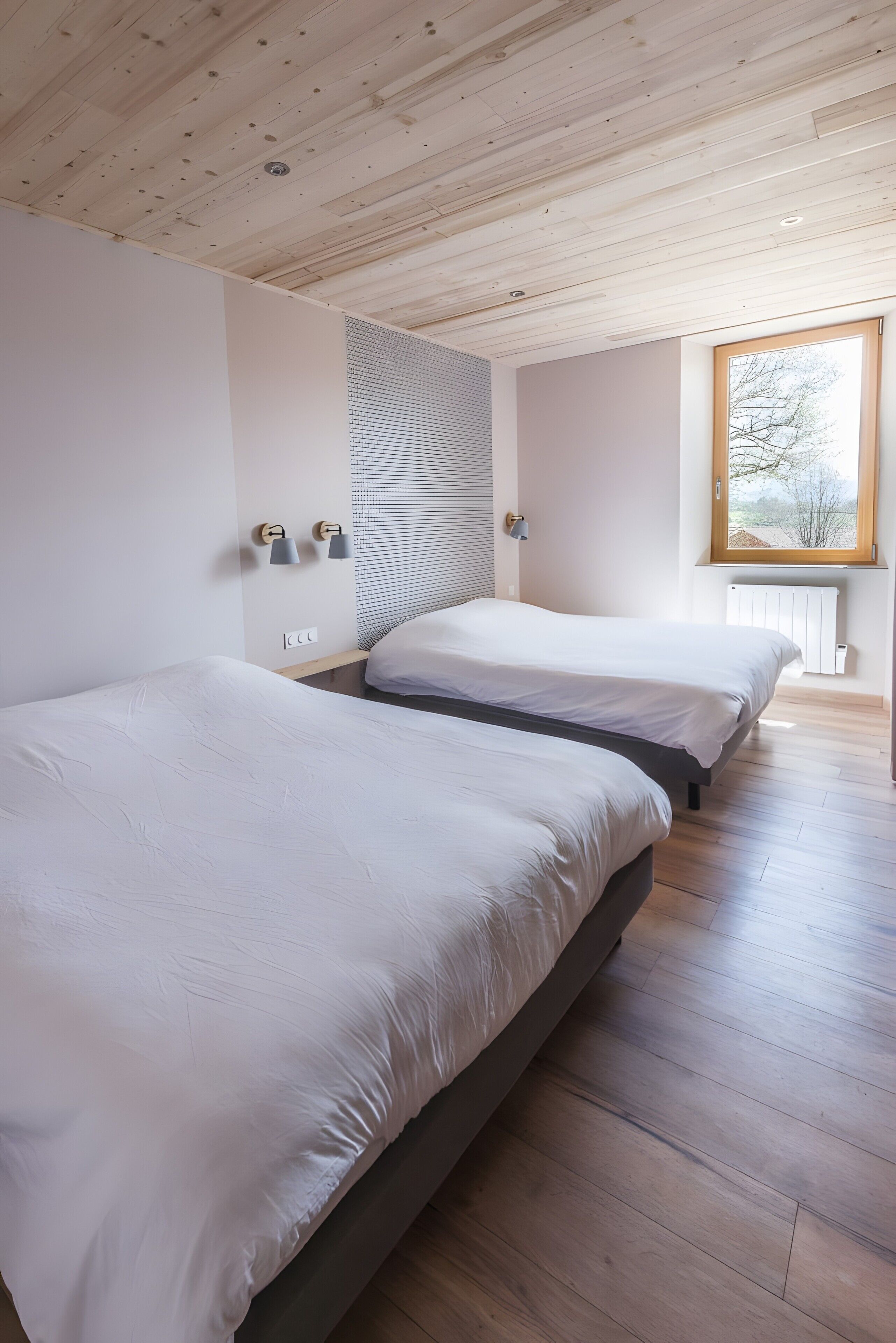 A bedroom with two beds, wooden flooring, a sloped ceiling, and a window with a view.
