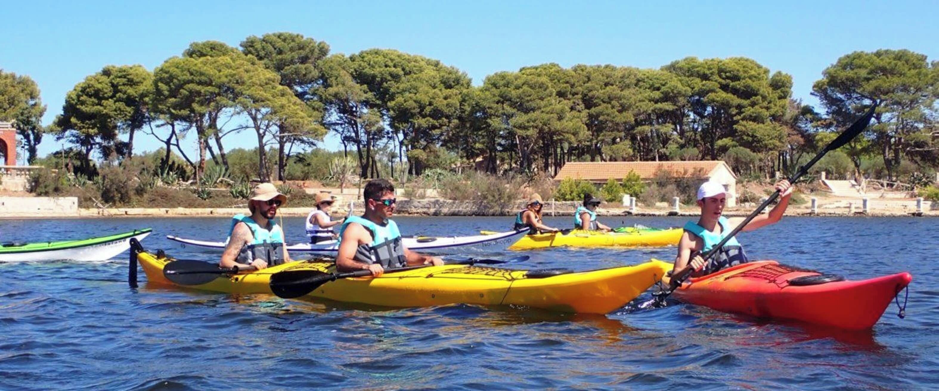 A group of people kayaking on a calm body of water with trees in the background.