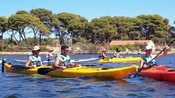 A group of people kayaking on a calm body of water with trees in the background.
