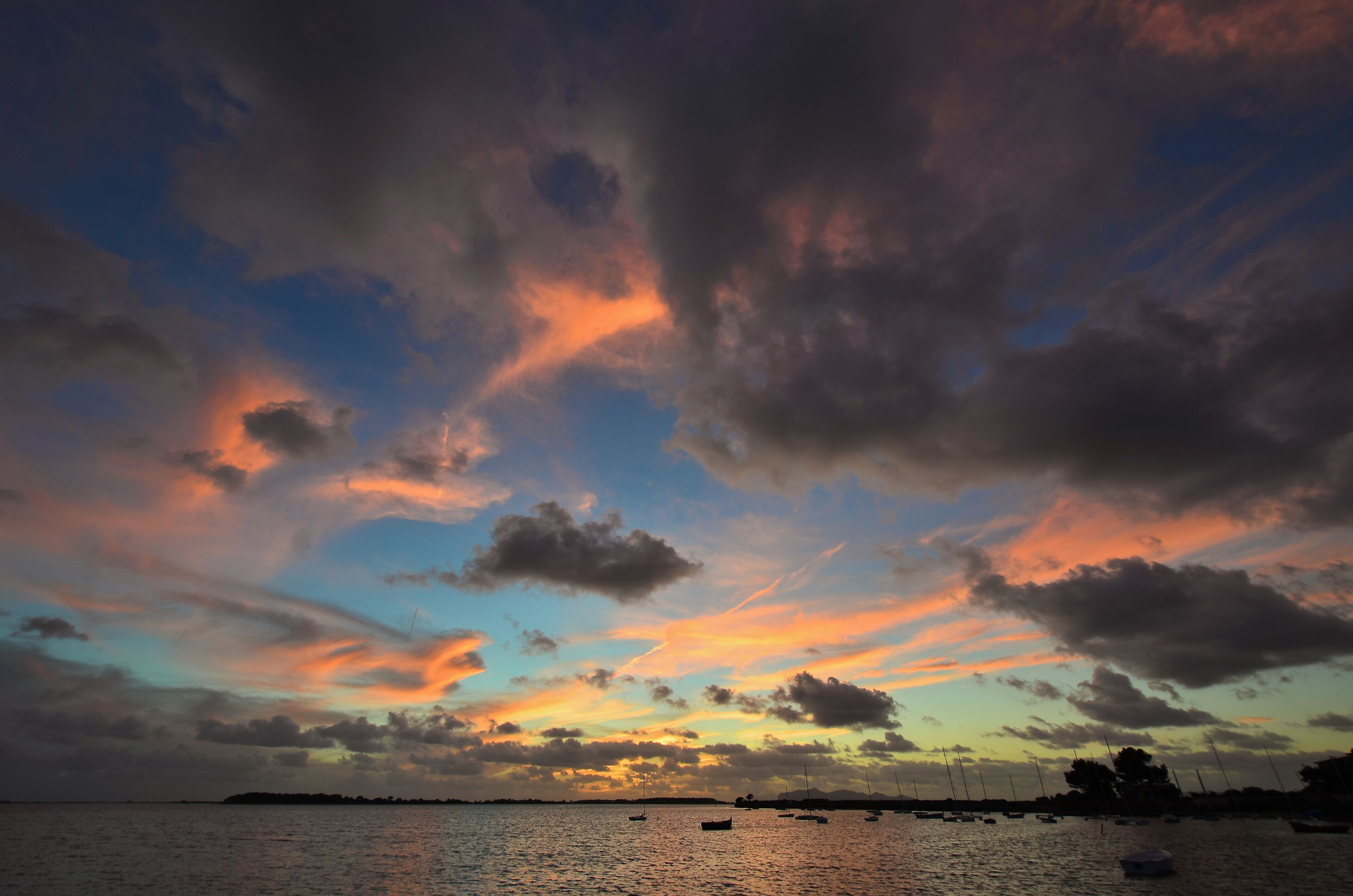 Un coucher de soleil sur une étendue d’eau, avec des bateaux.
