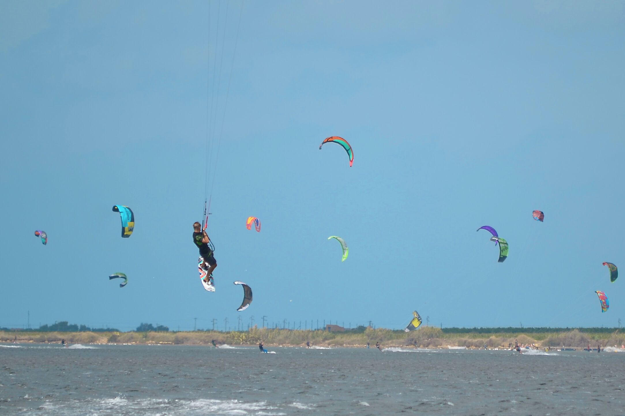 Ein Gewässer mit mehreren Drachen und einer Person, die parasailt.