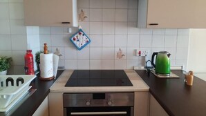 Une cuisine avec une plaque de cuisson noire, un four encastré et une bouilloire posée sur le plan de travail.