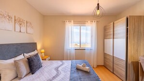 Une chambre à coucher comprenant un lit, une table de chevet, une lampe, une fenêtre avec des rideaux et une vue sur l’extérieur.