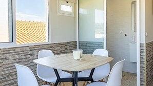 Une salle de conférence avec une table ronde, des chaises blanches, un verre de lait et une vue sur un toit recouvert de tuiles, visible à travers une fenêtre.