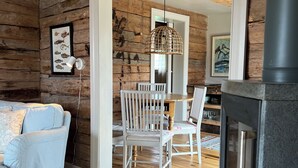 Un interior rústico con una pared de madera, una zona de comedor con sillas blancas, un sofá azul y una chimenea.