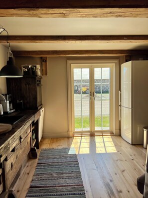 A kitchen with wooden floors, a refrigerator, a stove, and a window with a view of the outside. - Snickarboden – Cozy farmhouse living room near the woods and the lake (Kronobergs län)