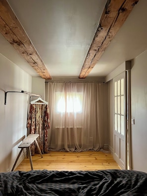A room with exposed wooden beams, a large window with sheer curtains, a wooden floor, and a whiteboard on the wall. - Snickarboden – Cozy farmhouse living room near the woods and the lake (Kronobergs län)