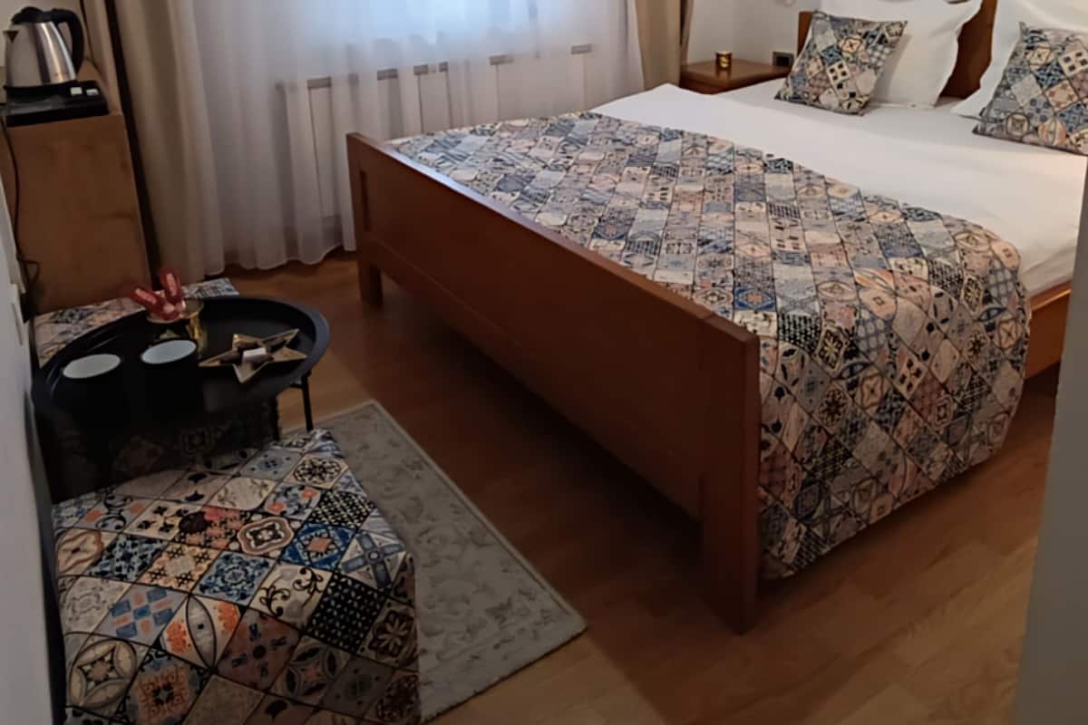 A bedroom with a large bed, a small table, a chair, and a radiator.
