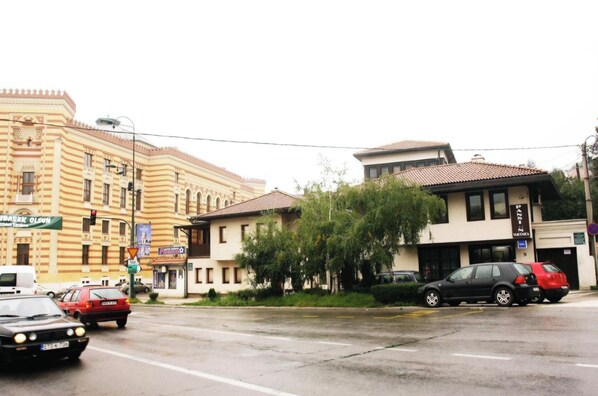 A street scene with buildings, cars, and a wet road. - Hotel Vijecnica (Sarajevo)