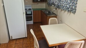 A compact kitchen with a refrigerator, oven, and sink. There is a dining table with chairs. - Cairns holiday unit apartment kitchen aircon wifi near esplanade and hospital (Cairns North)