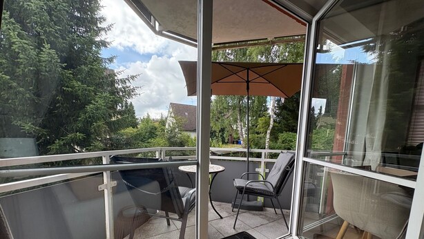 Un balcon avec une porte vitrée, une table, deux chaises et un tabouret en osier.