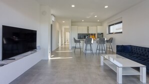 Een moderne woonkamer met een flatscreen televisie, een donkerblauwe bank en een witte salontafel.